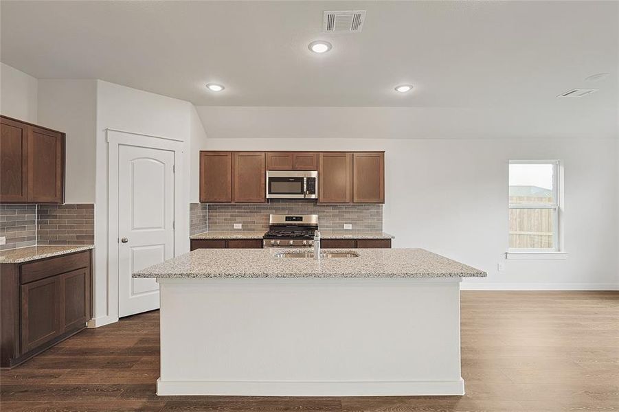 Kitchen featuring dark hardwood / wood-style floors, stainless steel appliances, sink, and an island with sink