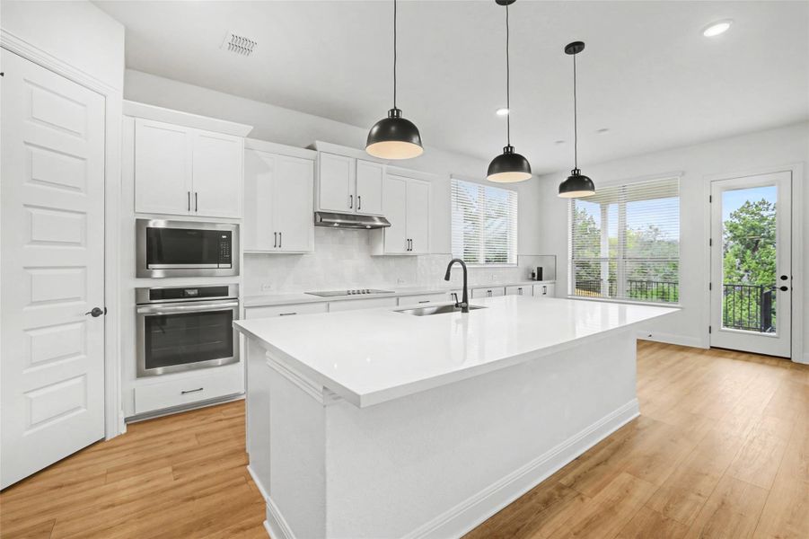 Kitchen featuring stainless steel appliances, white cabinetry, light wood-style flooring, and decorative light fixtures