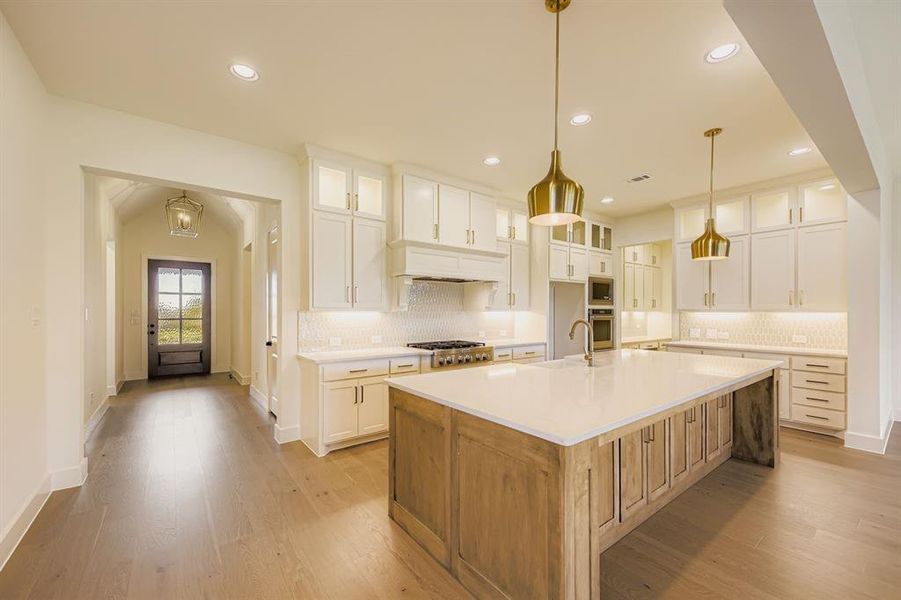 Kitchen with glass insert cabinets, a kitchen island with sink, white cabinets, and recessed lighting