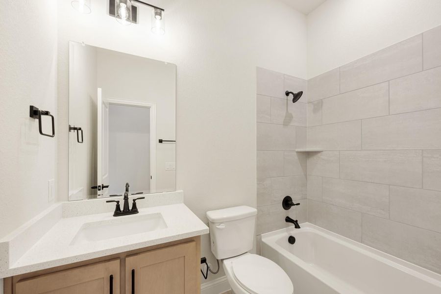 Bathroom with white quartz vanity, tub-shower combo with large tile surround, and matte black fixtures