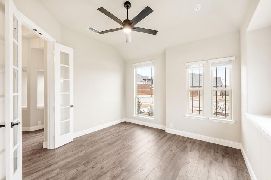Empty bedroom with hardwood floors, ceiling fan, two windows, and French doors leading to hallway Empty bedroom with hardwood floors, ceiling fan, two windows, and French doors leading to hallway