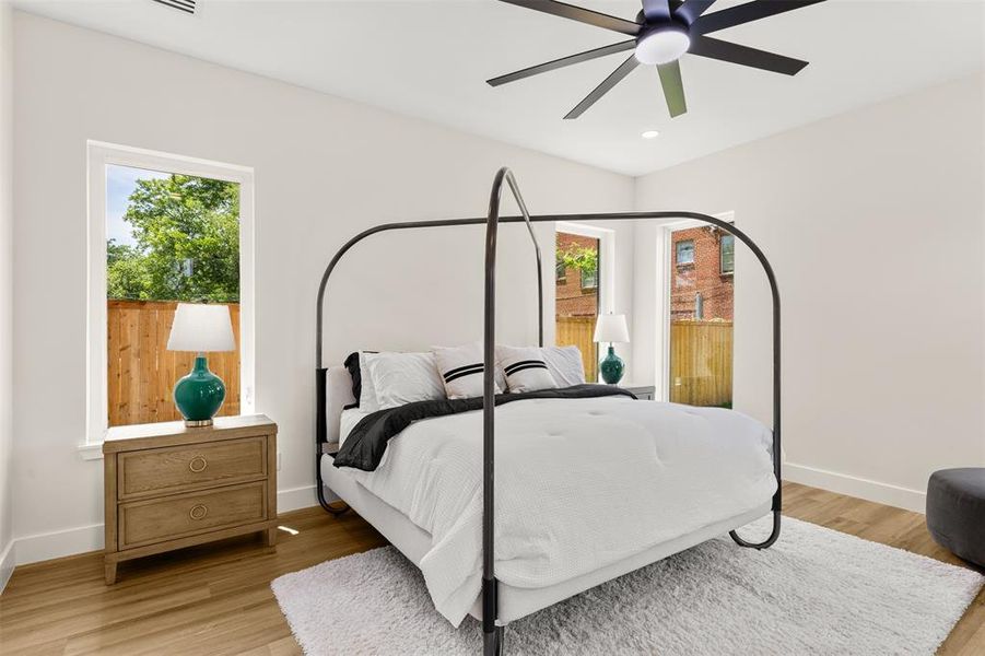 Spacious bedroom with wood-finish flooring, two large windows, recessed lighting, and a contemporary ceiling fan
