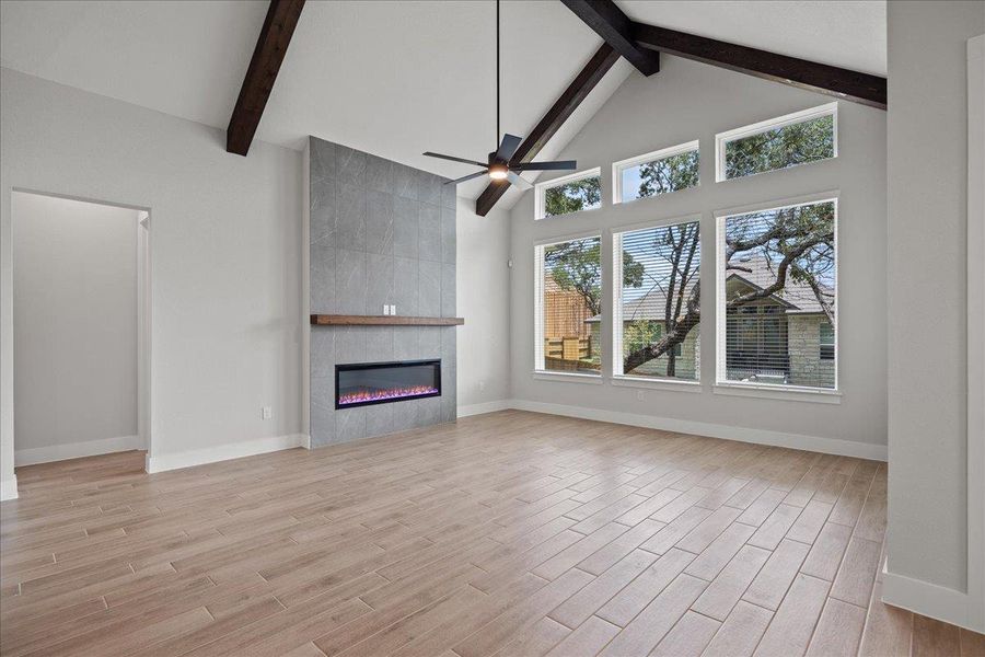 Unfurnished living room with high vaulted ceiling, beam ceiling, a fireplace, light wood-style flooring, and ceiling fan Unfurnished living room with high vaulted ceiling, beam ceiling, a fireplace, light wood-style flooring, and ceiling fan