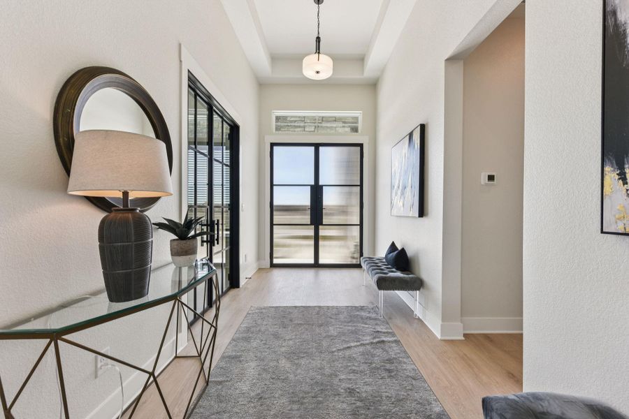 Foyer with light wood-style flooring, a raised ceiling, and a textured wall
