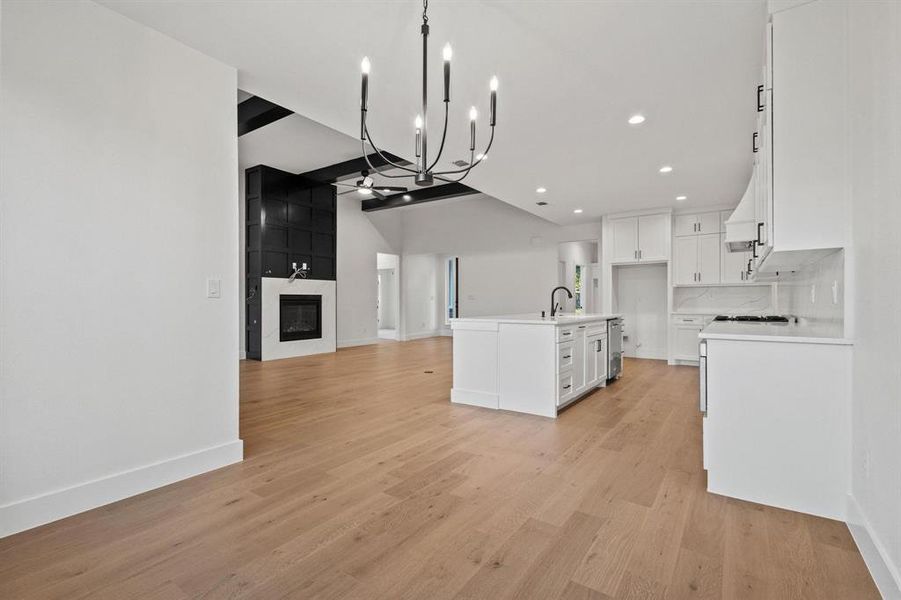 Kitchen with open floor plan, a fireplace, a chandelier, light wood-style flooring, and white cabinets