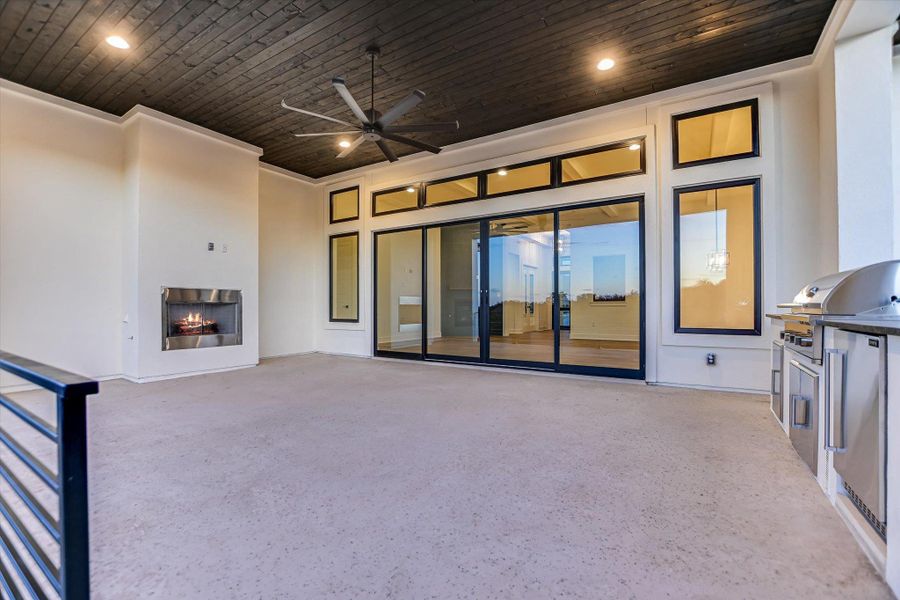 View of patio featuring a lit fireplace, area for grilling, and ceiling fan