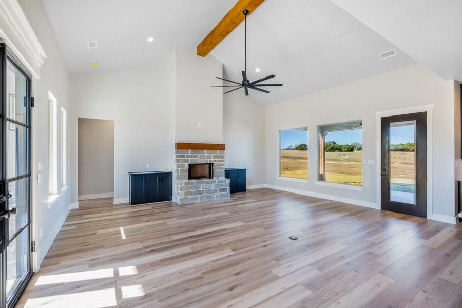 Unfurnished living room with a stone fireplace, ceiling fan, beamed ceiling, and high vaulted ceiling