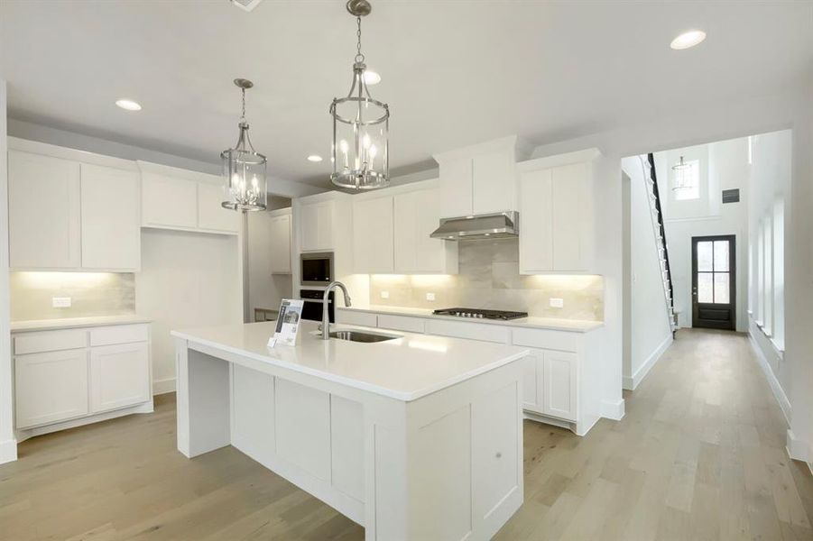 Modern kitchen featuring white cabinetry, light-toned wood-finish flooring, and a central island with a sink
