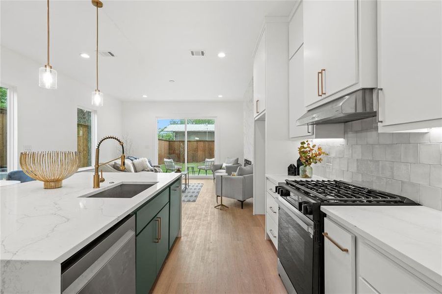 Kitchen featuring under cabinet range hood, stainless steel dishwasher, a sink, black gas range, and open floor plan