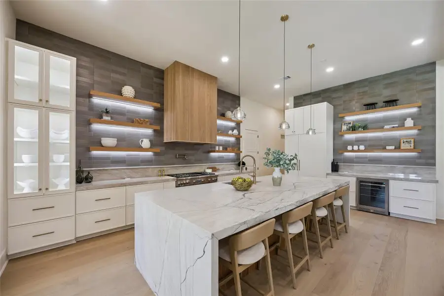 KITCHEN: Designed for both everyday living and entertaining, the chef's kitchen features Taj Mahal Quartzite countertops and premium Thermador appliances including a 6-burner gas range with integrated griddle, a convenient pot filler, illuminated shelving, and glass-front cabinetry.