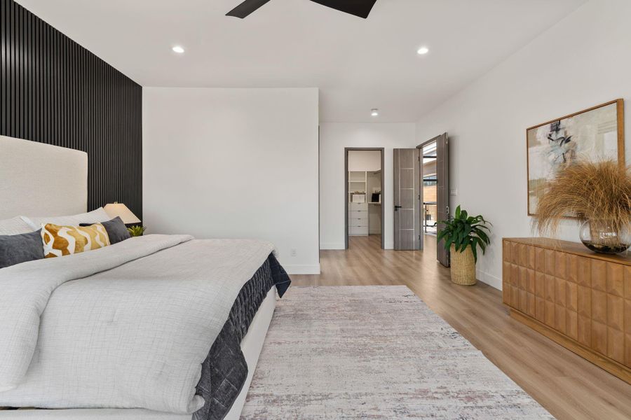 The full 25-by-17-foot scale of the primary suite reads clearly from this angle — wide-plank vinyl flooring, clean white walls, and a wide opening on the far wall that leads directly to the walk-in closet and primary bath.