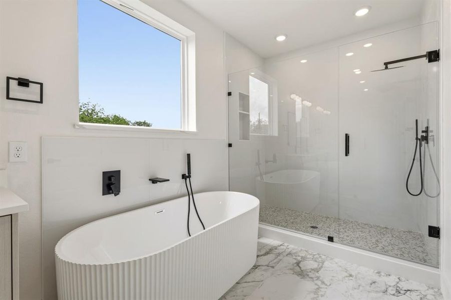 The bathroom features a modern freestanding tub, a spacious glass-enclosed shower with a pebble floor, and large format marble-look floor tiles