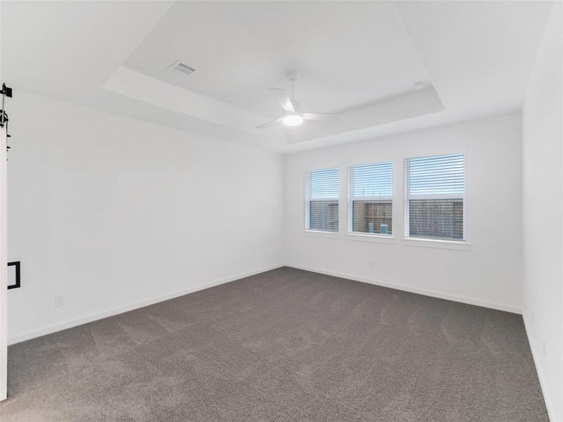 Primary bedroom with neutral carpet, a ceiling fan, and three large windows allowing natural light.