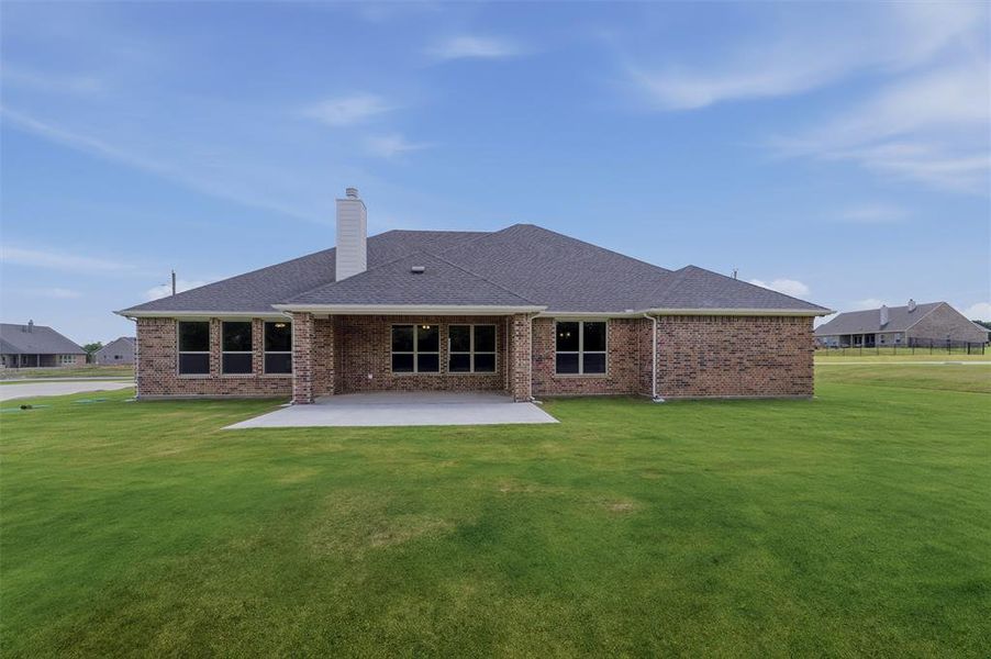 Expansive backyard featuring a large concrete patio, brick exterior, multiple windows with dark framing, a prominent chimney, and a dark shingle roof Expansive backyard featuring a large concrete patio, brick exterior, multiple windows with dark framing, a prominent chimney, and a dark shingle roof