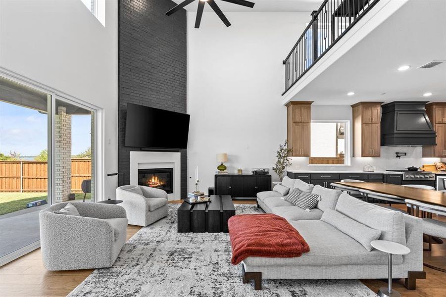 Living area featuring a towering ceiling, light wood finished floors, a fireplace, and a ceiling fan Living area featuring a towering ceiling, light wood finished floors, a fireplace, and a ceiling fan