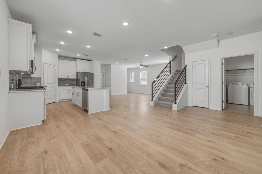 Kitchen with open floor plan, a kitchen island with sink, stainless steel appliances, white cabinets, and light wood-style flooring