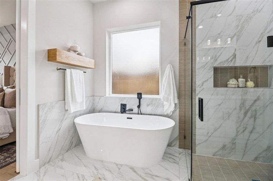 Freestanding soaking tub with black matte fixtures, set against large format marble-look tile flooring and wainscoting