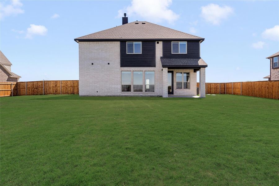 Two-story home rear view with brick exterior, dark siding accents, covered patio, and large fenced backyard with green lawn. Two-story home rear view with brick exterior, dark siding accents, covered patio, and large fenced backyard with green lawn.