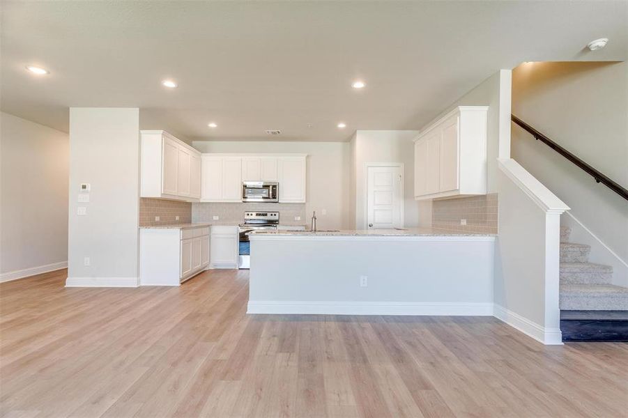 Kitchen featuring light stone counters, tasteful backsplash, stainless steel appliances, light hardwood / wood-style floors, and white cabinets