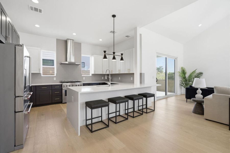 Kitchen featuring a kitchen bar, high quality appliances, light wood-style flooring, two tone cabinetry, and backsplash