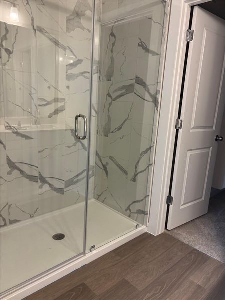 Full bath with a marble finish shower and wood finished floors