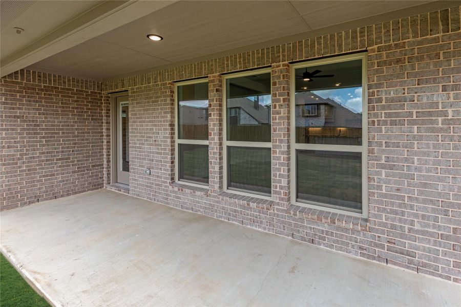 Covered back patio with concrete floor and brick exterior wall with two large windows and a door Covered back patio with concrete floor and brick exterior wall with two large windows and a door