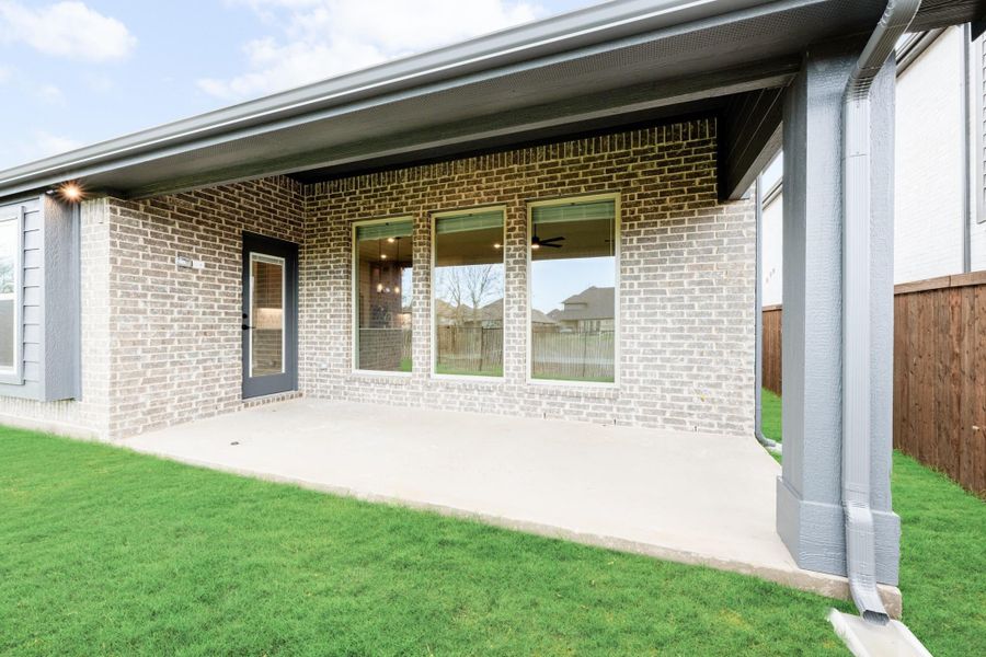 Covered back patio with concrete slab, brick exterior, large windows, and green lawn