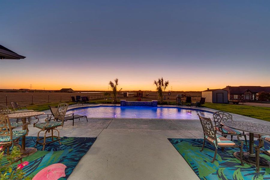 Pool at dusk with pool water feature, a patio area, a storage shed, and a lawn
