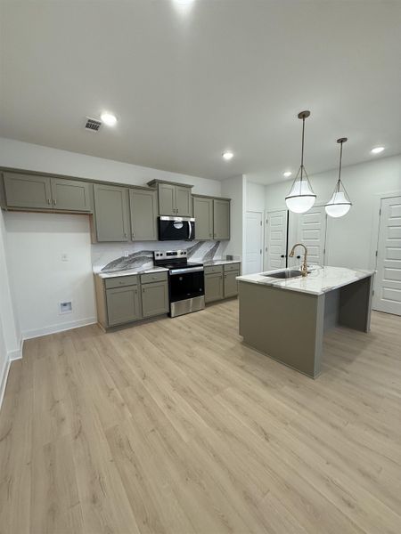 Kitchen featuring gray cabinetry, stainless steel appliances, hanging light fixtures, light wood-style floors, and a center island with sink