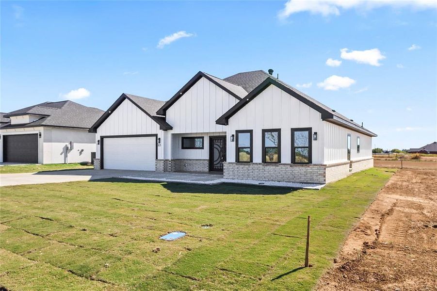 Modern farmhouse style home with concrete driveway, a front yard, brick siding, board and batten siding, and a garage Modern farmhouse style home with concrete driveway, a front yard, brick siding, board and batten siding, and a garage