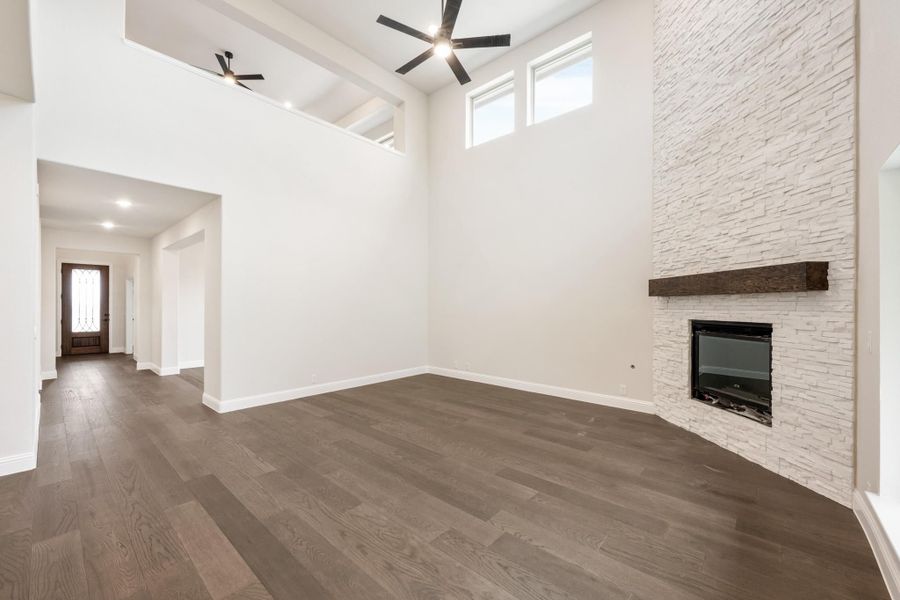 Open living room with vaulted ceiling, stone fireplace, wood mantel, and dark hardwood floors Open living room with vaulted ceiling, stone fireplace, wood mantel, and dark hardwood floors