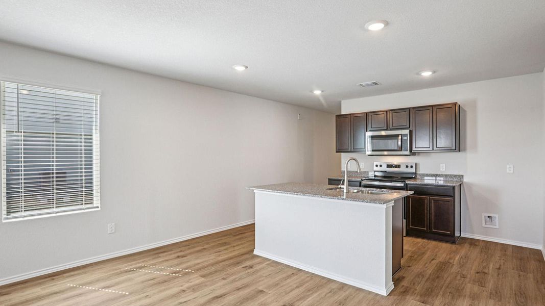 Kitchen with dark wood finish cabinets, light stone countertops, stainless steel appliances, light wood-type flooring, and recessed lighting