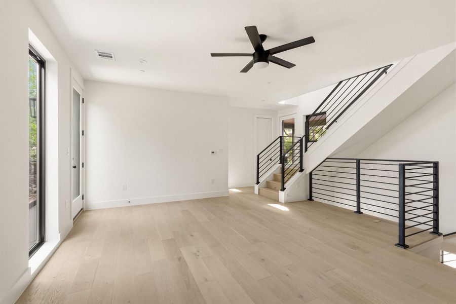Spacious open-concept room featuring light wood-finish flooring, a modern black ceiling fan, and white walls