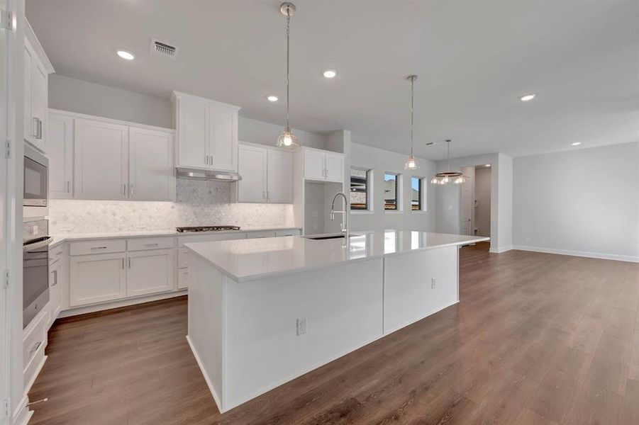 Kitchen with white cabinets, a kitchen island with sink, dark wood-style flooring, and hanging light fixtures