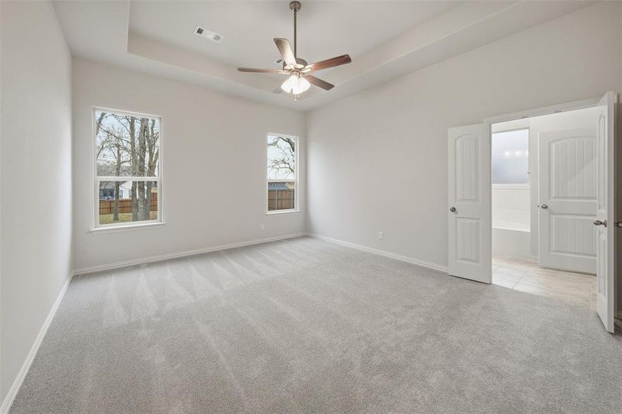 Empty room featuring light carpet, ceiling fan, and a tray ceiling Empty room featuring light carpet, ceiling fan, and a tray ceiling
