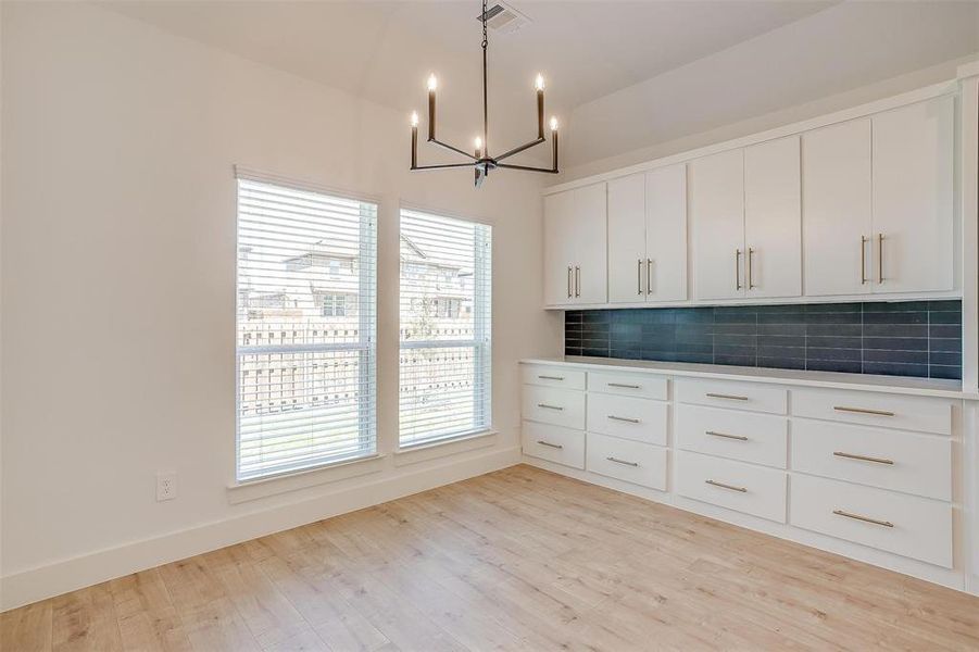 Kitchen with light hardwood / wood-style floors, an inviting chandelier, white cabinets, pendant lighting, and tasteful backsplash