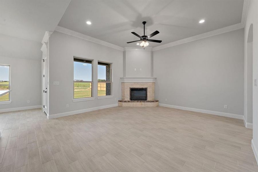 Unfurnished living room with light wood finished floors, a ceiling fan, crown molding, recessed lighting, and a brick fireplace