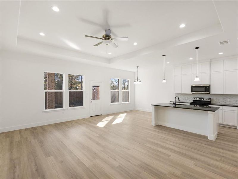Kitchen with open floor plan, a center island with sink, appliances with stainless steel finishes, white cabinetry, and a ceiling fan