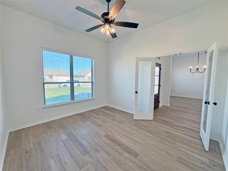 Spare room featuring light wood-type flooring, french doors, and a chandelier