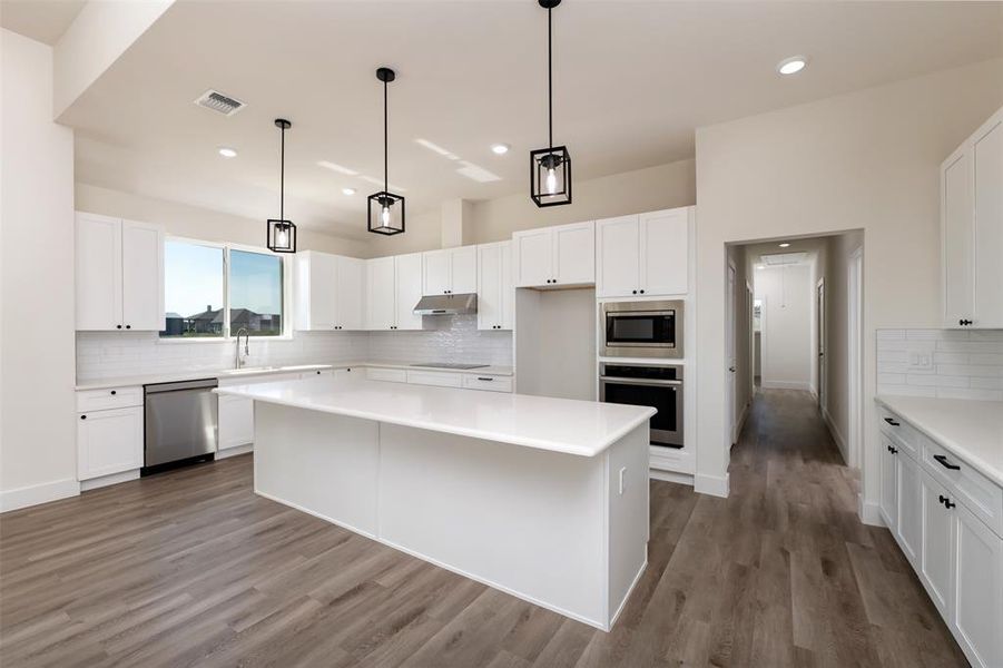 Kitchen with wood finished floors, under cabinet range hood, stainless steel appliances, visible vents, and decorative backsplash