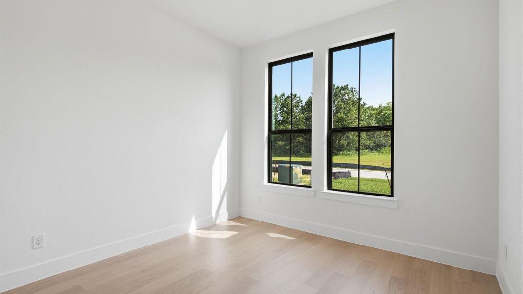A  third bedroom with two windows, decorated with bedroom furniture and wood flooring.