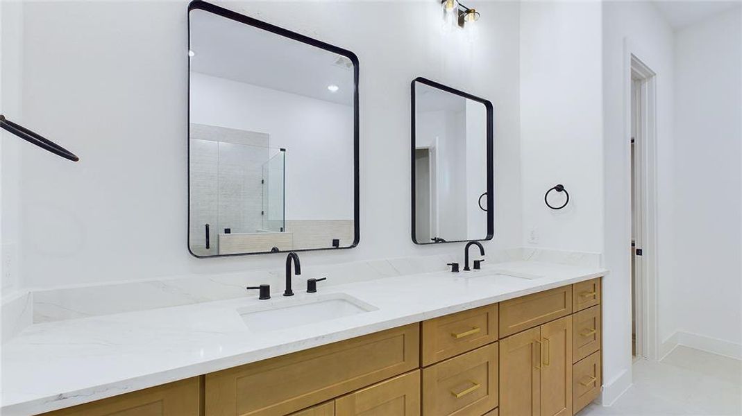 Primary bathroom offers a spacious dual vanity with under-mount sinks, and black faucets. Thoughtfully laid out cabinetry combines drawers with cabinets to leave no space wasted.