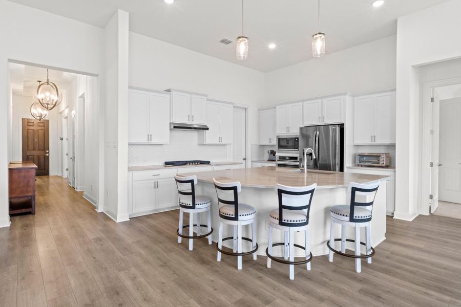 Bathed in natural light, the space boasts shaker-style white cabinetry, premium stainless steel appliances, and a massive curved granite island that serves as the ultimate social hub.