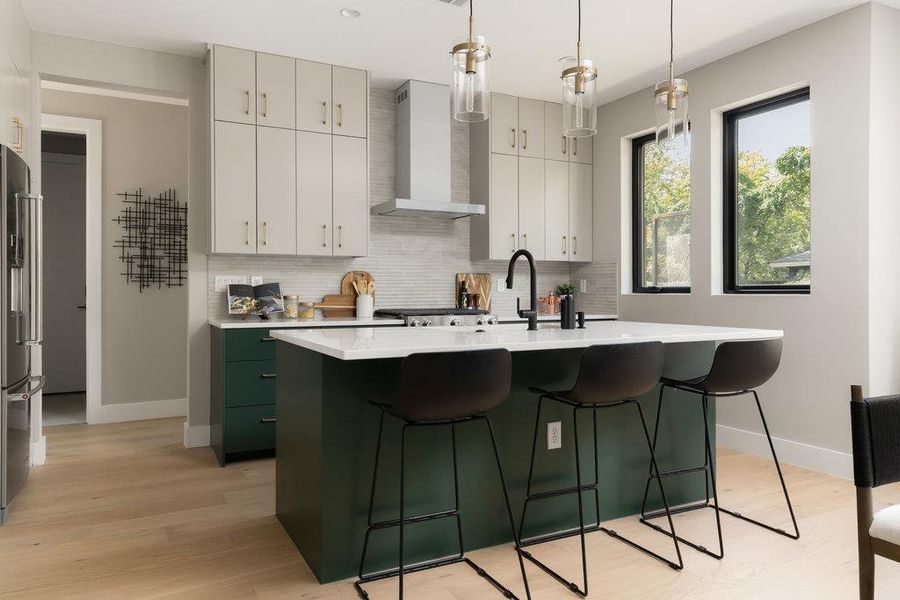 Kitchen featuring green cabinetry, an island with sink, decorative backsplash, pendant lighting, and wall chimney exhaust hood