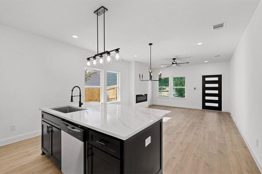 Kitchen featuring dark cabinets, hanging light fixtures, light wood finished floors, dishwasher, and light stone countertops