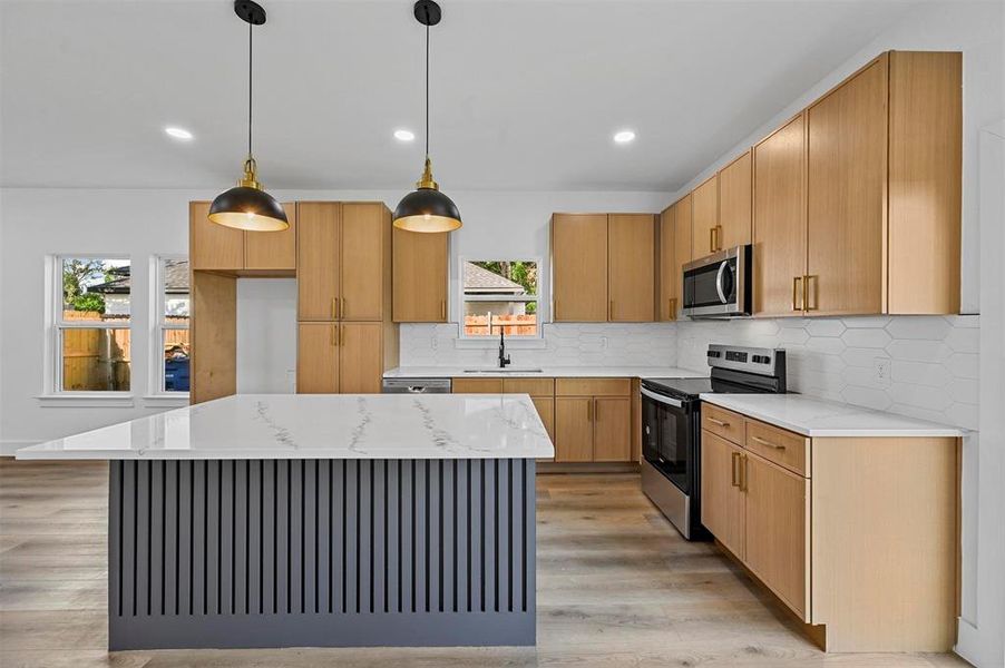 Kitchen with tasteful backsplash, stainless steel appliances, decorative light fixtures, light wood-type flooring, and a kitchen island