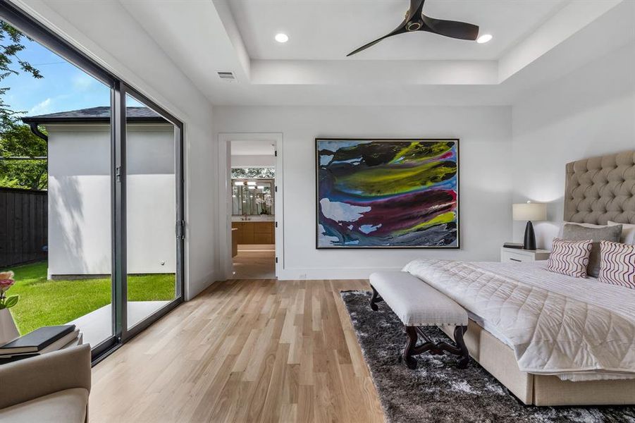 Bedroom featuring access to exterior, a tray ceiling, ceiling fan, light hardwood / wood-style floors, and ensuite bathroom