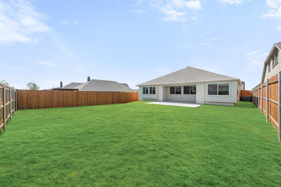 Backyard with large green lawn, wood privacy fence, and rear view of single-story home with covered patio Backyard with large green lawn, wood privacy fence, and rear view of single-story home with covered patio