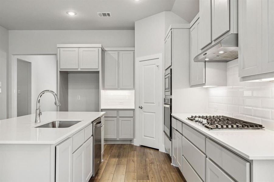 Kitchen featuring appliances with stainless steel finishes, decorative backsplash, sink, an island with sink, and light hardwood / wood-style floors