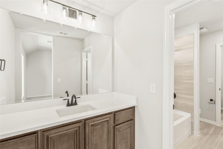 Bathroom vanity with white countertop, dark wood cabinets, large mirror, and view into soaking tub area Bathroom vanity with white countertop, dark wood cabinets, large mirror, and view into soaking tub area